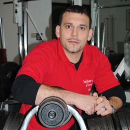 Eine Person in rotem Hemd lehnt sich an eine Hantel in einem Fitnessstudio.