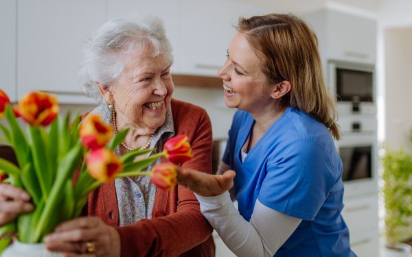 Eine Seniorin gestaltet voller Freude einen Blumentopf mit Tulpen zusammen mit ihrer Pflegekraft.