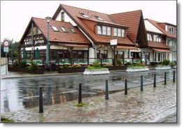 Eckhaus mit rotem Dach an nasser Straße, mehrere Fenster, kleines Straßencafé davor.