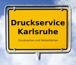 Gelbes Schild mit der Aufschrift „Druckservice Karlsruhe, Drucksachen und Werbeflächen“ vor Himmel.