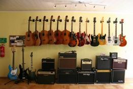 Gitarren an der Wand mit Verstärkern darunter. Verschiedene Modelle und Farben.