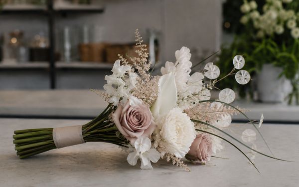 Moderner minimalistischer Blumenstrauß in Weiß, Creme und gedecktem Rosé auf dem Tresen eines Floristenladens.