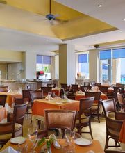 Restaurante elegante con mesas cubiertas de manteles naranjas y vista al mar.