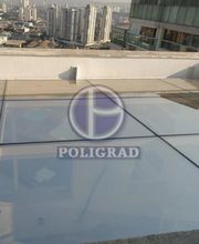 Terraço com piso de vidro, vista para cidade ao fundo e logotipo Poligrad refletido.