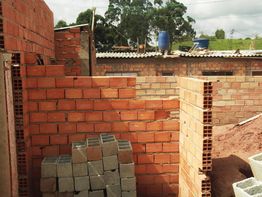Construção de parede de tijolos em andamento, com blocos empilhados no chão ao lado.