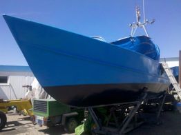Blaues Motorboot auf Stütze im Trockendock, mit glänzender Oberfläche, bei sonnigem Himmel.