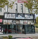 Tienda de muebles con fachada de cristal y anuncios en un edificio moderno.