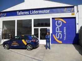 Taller mecánico "Talleres Lidermotor" con coche azul y persona en uniforme azul al frente.