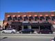 Brick building with orange awnings, parked cars in front on a clear day.