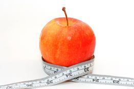 Roter Apfel mit Maßband umwickelt, Symbol für gesunde Ernährung.