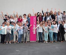 Gruppe von Frauen posiert fröhlich mit erhobenen Armen vor einem "müller MODE"-Schild.