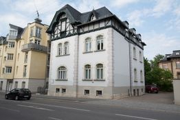 Weiße zweistöckige Altbauvilla mit schwarzen Akzenten an einer städtischen Straße.