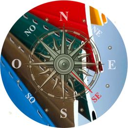 Brújula sobre folletos de colores azul, rojo y verde. Indicaciones cardinales visibles.