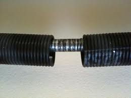 Close-up of a broken black garage door spring on a white background.