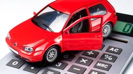 Red toy car with an open door on a calculator, symbolizing car expenses or budgeting.