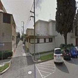 Narrow urban street with parked cars, buildings, and a tree-lined sidewalk on a clear day.