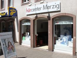 Geschäftsfassade des Hörcenters Merzig mit zwei Fenstern und einem Eingang bei Sonnenschein.