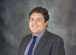 Smiling man in a suit and tie against a gray studio background.