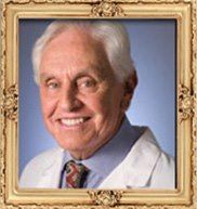Elderly man smiling in a gold ornate frame, wearing a white coat and tie.