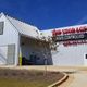 Storage facility with red sign, metal exterior, tree, and blue sky in the background.