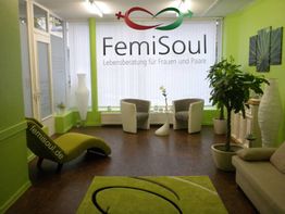Grün eingerichteter Beratungsraum mit Pflanzen, Sesseln und dem Schriftzug "FemiSoul" an der Wand.