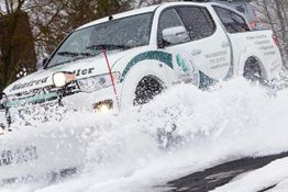 Ein weißer Schneepflug räumt Schnee von einer Straße.