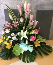 Arreglo floral con lirios rosas y blancos, orquídeas amarillas y hojas verdes sobre el suelo.