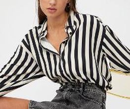 Mujer sentada con camisa de rayas blancas y negras, y falda gris. Fondo blanco.