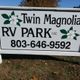 Sign for Twin Magnolia RV Park with phone number and magnolia flower graphics.