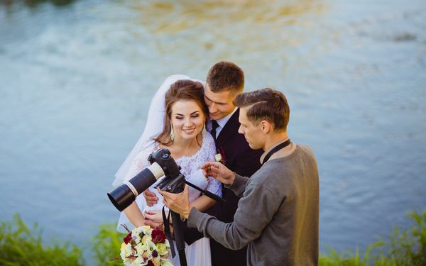 Fotograf zeigt Hochzeitspaar Bilder auf seiner Kamera vor einem See