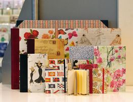 Mehrere Notizbücher mit bunten, floralen und künstlerischen Umschlägen auf einem Tisch ausgestellt.