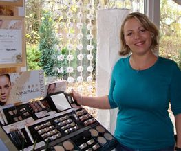 Eine Frau steht lächelnd neben einem Kosmetikdisplay mit verschiedenen Make-up-Produkten.