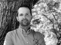 Man leaning against tree in black and white, with blurred foliage background.