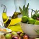Caraffa di olio d'oliva con ciotola di olive verdi e nere su un tavolo, vicino a pane e cucchiaio.