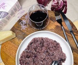 Lila Risotto mit Radicchio, Rotweinglas, Käse und Besteck auf einem Holzbrett.