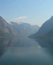 Ein ruhiger Fjord, umgeben von hohen, felsigen Bergen unter klarem, blauem Himmel.