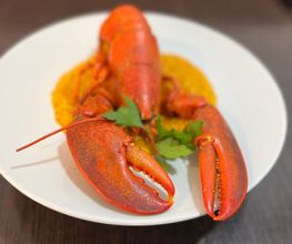 Langosta cocinada servida en un plato blanco con guarnición de perejil sobre salsa amarilla.