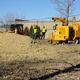 Construction workers and equipment near a large pile of dirt beside a yellow machine.