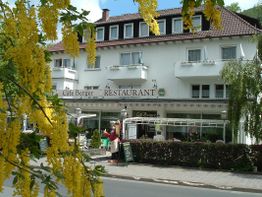 Zweistöckiges Gebäude mit "Café Berger" Schild, gelbe Blumen im Vordergrund, Sommerstimmung.