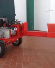 Spaccalegna rosso con motore su ruote, posizionato su un pavimento di piastrelle marroni.