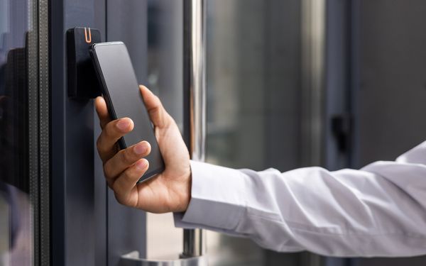 Mann entsperrt mit seinem Handy den Zugang zu einem Bürogebäude. 
