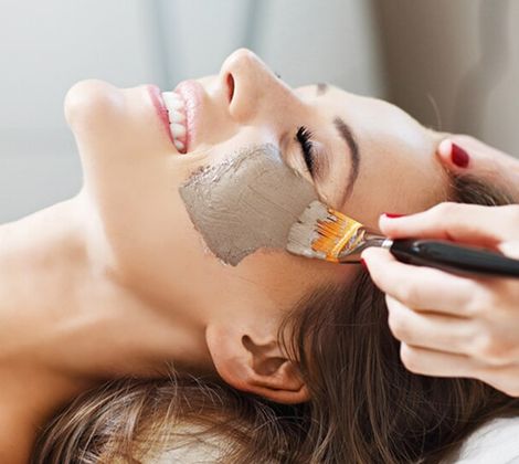 Donna sorridente riceve maschera di fango sul viso in un salone di bellezza.