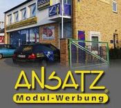 Ein Bürogebäude mit Auto, Werbung von "ANSATZ Modul-Werbung" in gelber Schrift auf Grau.