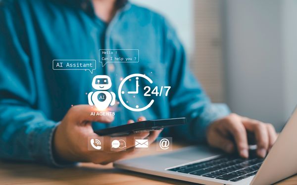 Person arbeitet am Laptop und Smartphone mit eingeblendeten Symbolen für KI-Assistenten und digitale Kommunikation.