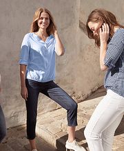 Drei Frauen in legerer Kleidung stehen draußen und unterhalten sich vor einer weißen Wand.