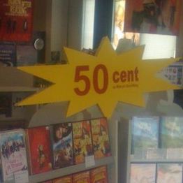 Ein gelbes Schild in Sternform mit rotem Text: "50 cent" über DVDs in einem Laden.