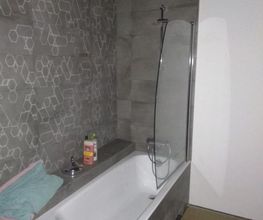 Baño moderno con bañera, toalla doblada, y productos en el borde. Pared con diseño geométrico.