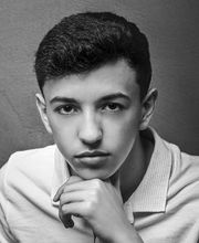 Joven con camisa blanca posa pensativo con la barbilla apoyada en la mano.