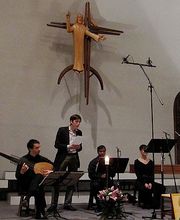Eine Gruppe musiziert in einer Kirche unter einem großen Kruzifix.