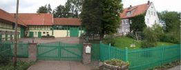 Ein Bauernhof mit roten Dächern, grünem Tor und Zäunen, umgeben von Bäumen und einem Garten.